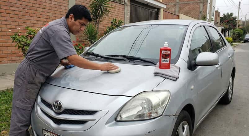 Aplicación manual de cera automotriz SONAX con almohadilla en un auto sedán