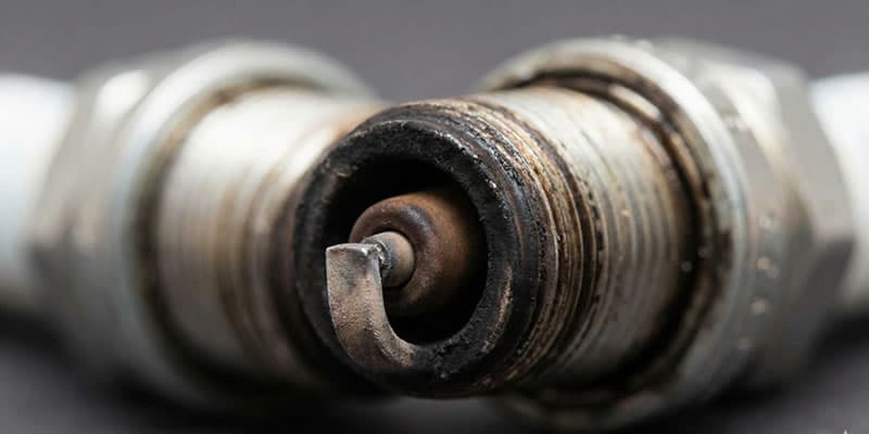 Primer plano de una bujía de motor usada y desgastada, con depósitos de carbón negro y el electrodo central erosionado.