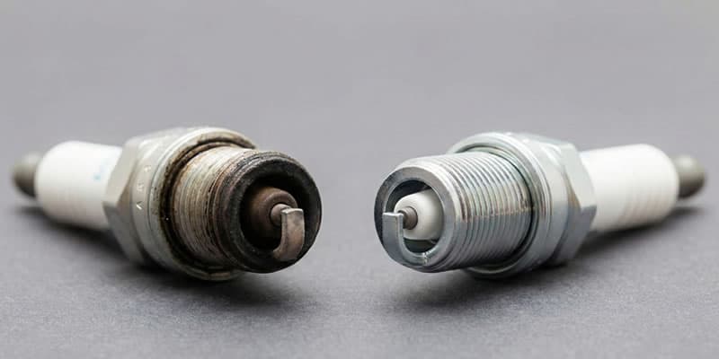 cambio bujías autos- omparación lado a lado de una bujía vieja y desgastada a la izquierda frente a una bujía nueva y limpia a la derecha.