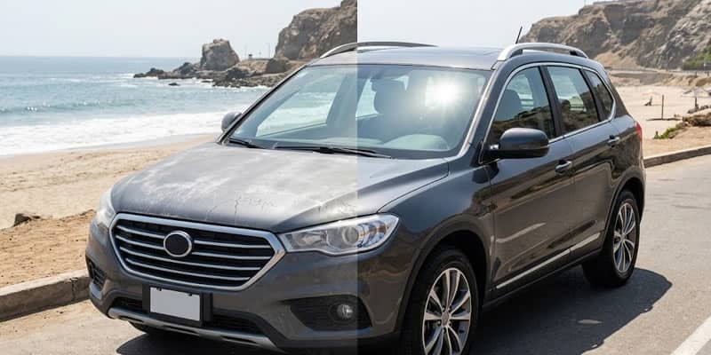 Fotografía de pantalla dividida de un SUV gris oscuro estacionado en una carretera costera junto a una playa bajo un sol brillante. La mitad izquierda de la imagen muestra la pintura del vehículo con un aspecto opaco, descolorido y con una capa blanquecina y agrietada de residuos de salitre y polvo, indicando daño ambiental. La mitad derecha muestra la misma sección del vehículo con la pintura en perfectas condiciones, con un brillo intenso y vibrante que refleja el sol y el cielo, demostrando un acabado protegido y encerado. El fondo muestra la playa, el océano y acantilados rocosos.